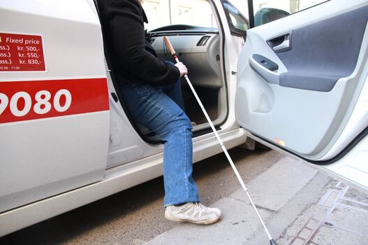 Bilde av person med hvit stokk på vei ut av en hvit bil.